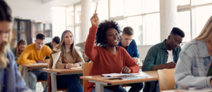 Happy student raising her hand to ask a question during lecture in the classroom.